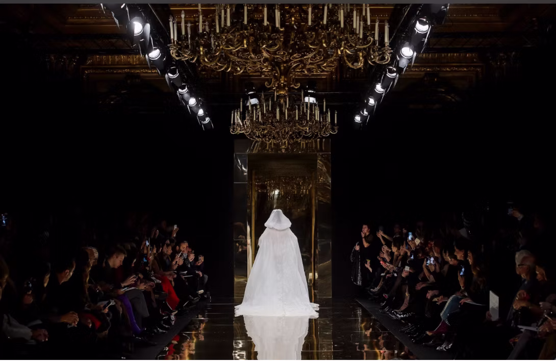 White bridal silhouette on a reflective runway beneath chandeliers